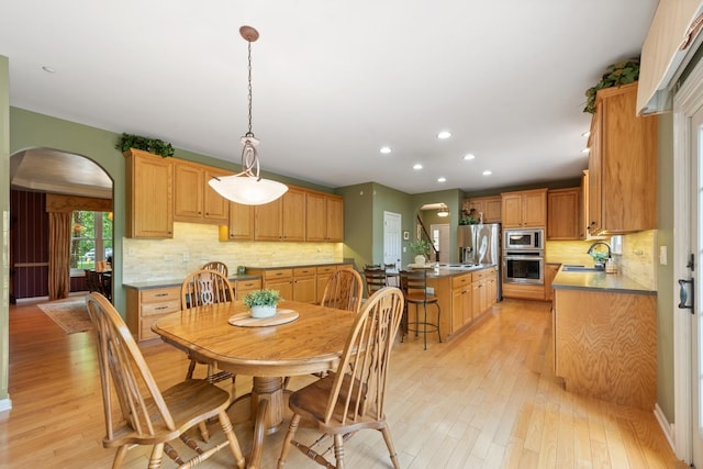 dining space with arched walkways, light wood-type flooring, and recessed lighting