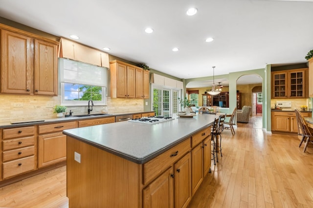 kitchen featuring a sink, arched walkways, a kitchen island, white gas cooktop, and tasteful backsplash