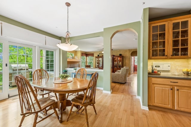 dining space with light wood-style flooring, arched walkways, and baseboards