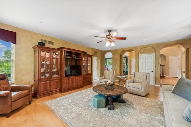 living area featuring arched walkways, light wood finished floors, and a ceiling fan