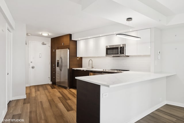 kitchen featuring white cabinets, light wood-type flooring, kitchen peninsula, appliances with stainless steel finishes, and tasteful backsplash