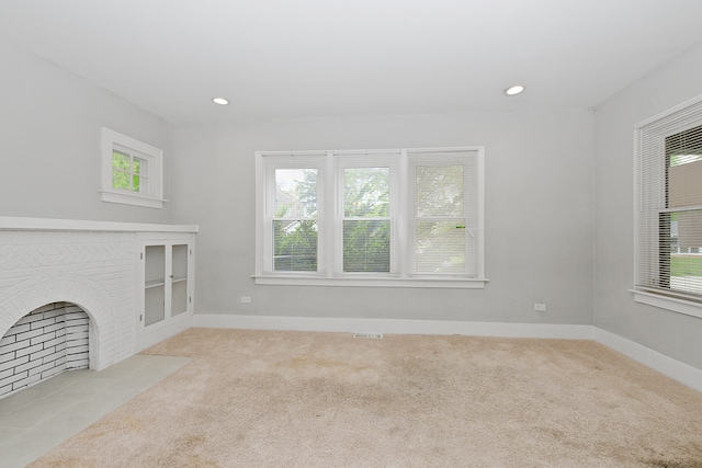 unfurnished living room featuring light carpet, a wealth of natural light, and a brick fireplace