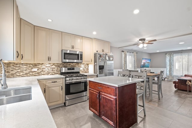 kitchen featuring ceiling fan, appliances with stainless steel finishes, a kitchen bar, cream cabinetry, and sink