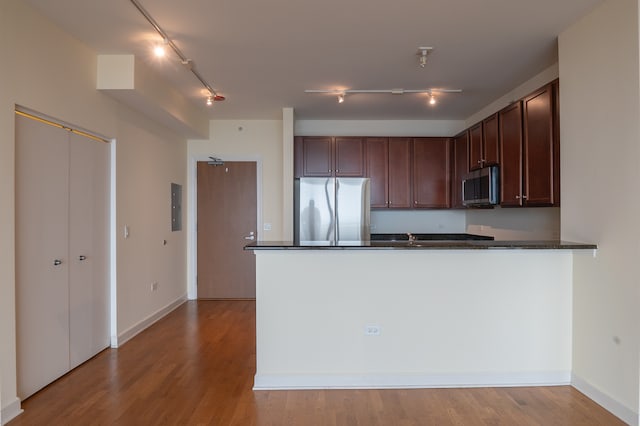 kitchen featuring appliances with stainless steel finishes, rail lighting, wood-type flooring, and kitchen peninsula