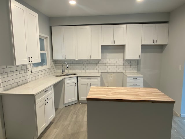 kitchen with light wood-type flooring, backsplash, wood counters, sink, and white cabinetry