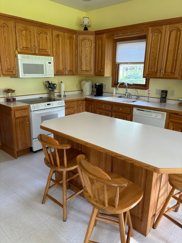 kitchen featuring sink, a breakfast bar, light tile flooring, and white appliances