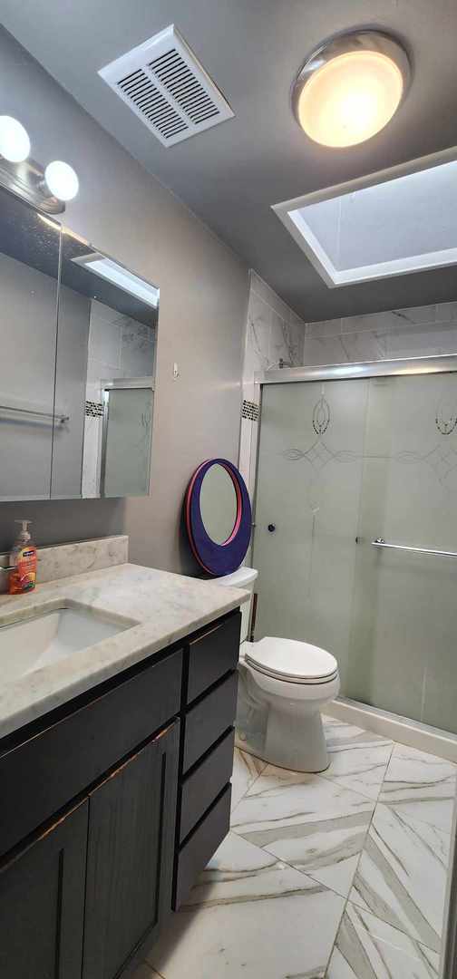 bathroom with a shower with shower door, tile flooring, vanity, and toilet