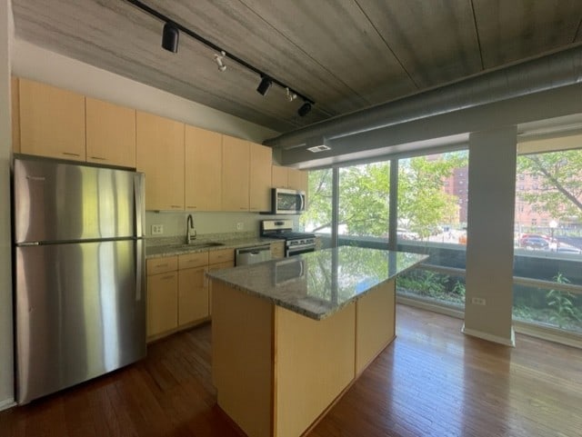 kitchen featuring appliances with stainless steel finishes, hardwood / wood-style flooring, light stone countertops, a kitchen island, and sink