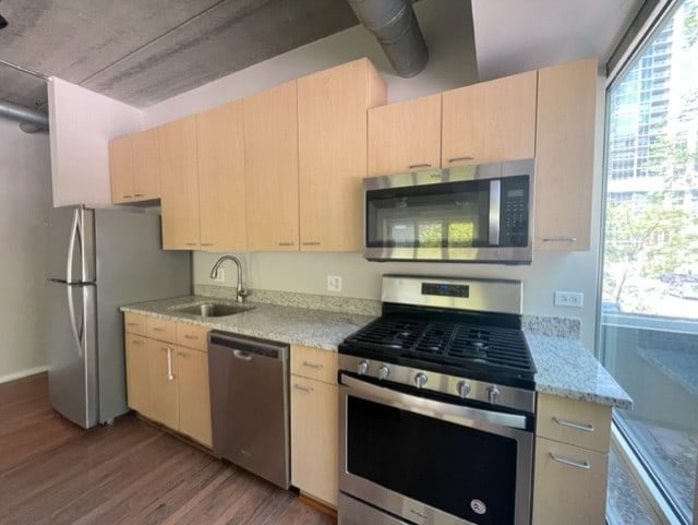 kitchen with appliances with stainless steel finishes, sink, light wood-type flooring, light brown cabinets, and light stone countertops