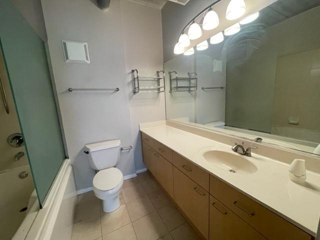 full bathroom featuring vanity, bath / shower combo with glass door, tile patterned flooring, and toilet