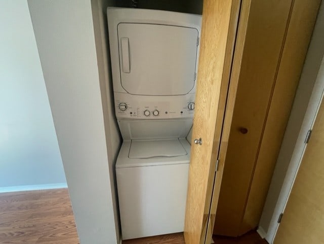 laundry area with hardwood / wood-style flooring and stacked washer / drying machine