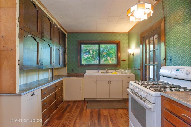 kitchen with stainless steel counters, a sink, dark wood-style flooring, wallpapered walls, and white gas range