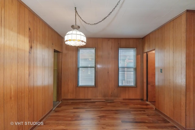 unfurnished dining area featuring wooden walls, wood finished floors, and baseboards