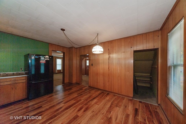 kitchen with brown cabinetry, wooden walls, freestanding refrigerator, and dark wood finished floors