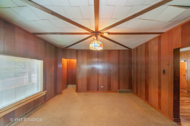 spare room with beamed ceiling, wooden walls, and light carpet