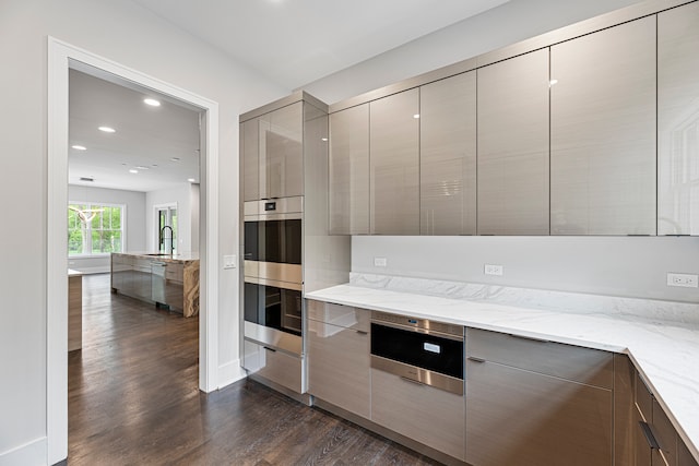 kitchen with double oven, dark wood-type flooring, light stone counters, and white dishwasher