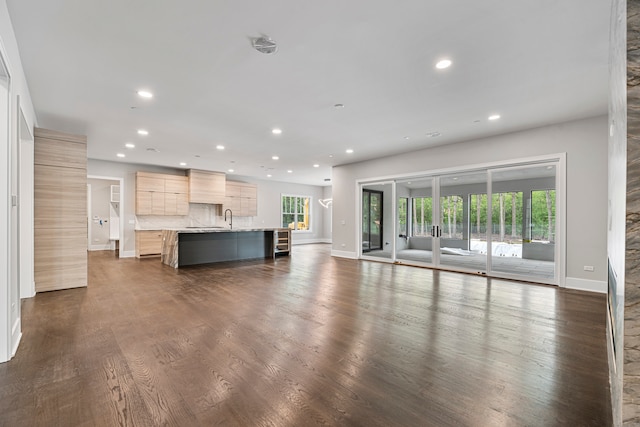 unfurnished living room featuring sink, dark wood-type flooring, and a healthy amount of sunlight