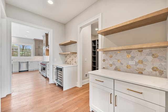 kitchen featuring wine cooler, backsplash, stainless steel appliances, light stone countertops, and light hardwood / wood-style floors