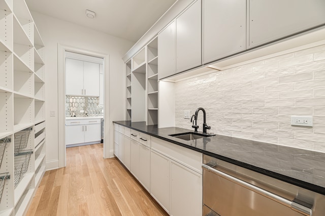 kitchen featuring light wood-type flooring, tasteful backsplash, sink, white cabinets, and stainless steel dishwasher