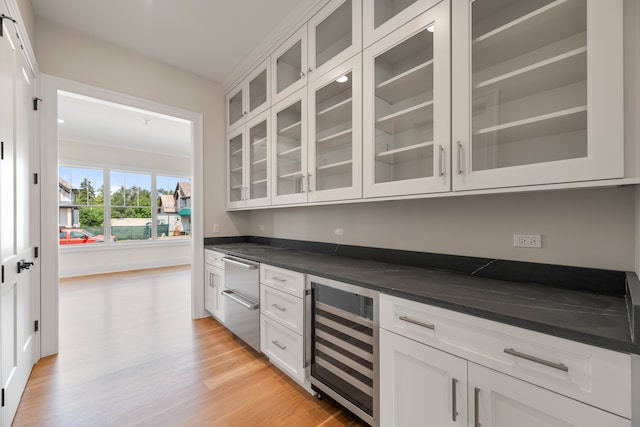 bar with light wood-type flooring, dark stone counters, beverage cooler, and white cabinets