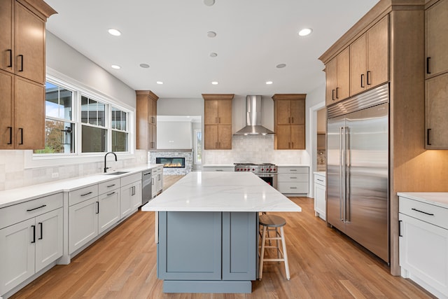 kitchen with tasteful backsplash, premium appliances, light hardwood / wood-style flooring, wall chimney range hood, and a center island