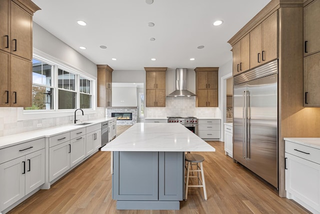kitchen with premium appliances, a sink, a kitchen island, wall chimney exhaust hood, and decorative backsplash