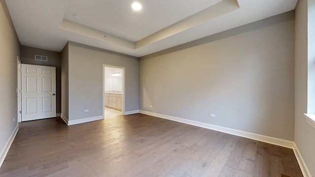 unfurnished bedroom with a tray ceiling, ensuite bath, and hardwood / wood-style floors