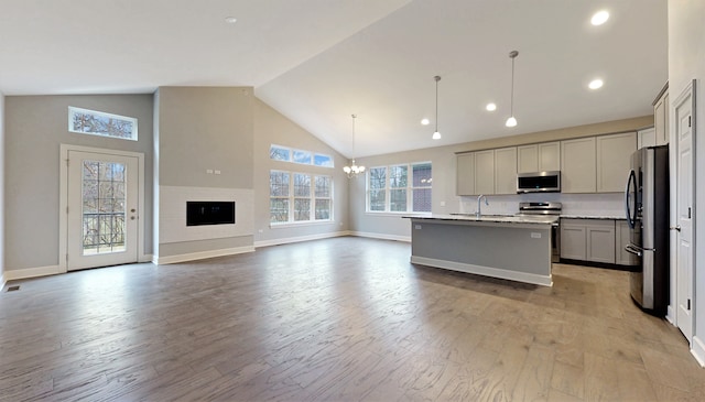 kitchen with light hardwood / wood-style flooring, a center island with sink, high vaulted ceiling, gray cabinetry, and appliances with stainless steel finishes