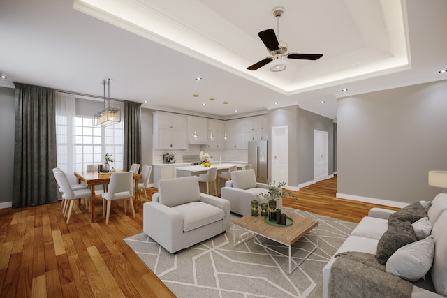 living room with ceiling fan, sink, light hardwood / wood-style flooring, and a tray ceiling