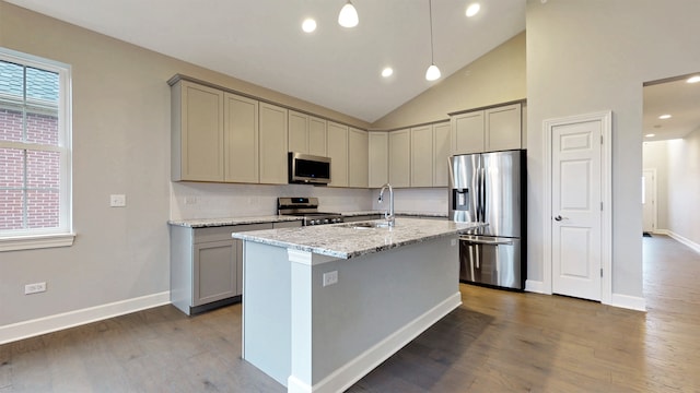 kitchen with stainless steel appliances, a center island with sink, hardwood / wood-style floors, light stone countertops, and pendant lighting