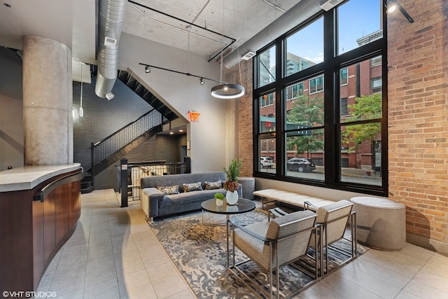 tiled living room featuring rail lighting, a towering ceiling, and brick wall