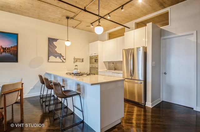 kitchen with hanging light fixtures, a kitchen breakfast bar, dark hardwood / wood-style flooring, stainless steel appliances, and white cabinets