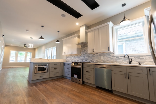 kitchen with decorative light fixtures, backsplash, wall chimney exhaust hood, hardwood / wood-style flooring, and appliances with stainless steel finishes