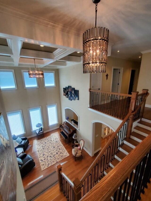 living room with coffered ceiling, beamed ceiling, crown molding, hardwood / wood-style floors, and a chandelier