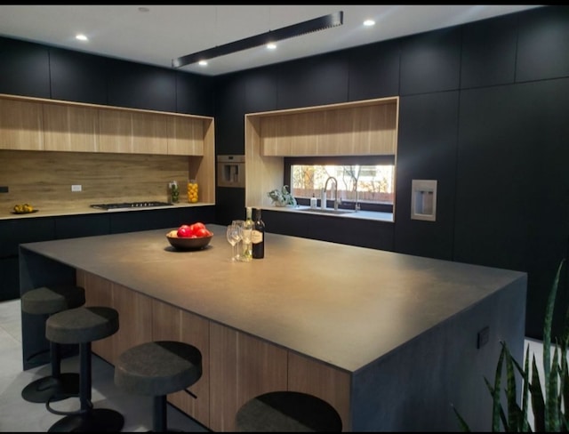 kitchen with decorative backsplash, a kitchen breakfast bar, gas stovetop, sink, and a large island