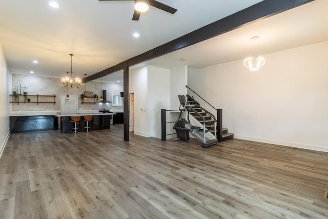 interior space featuring beamed ceiling, hardwood / wood-style flooring, ceiling fan with notable chandelier, and brick wall