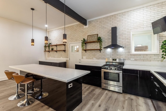 kitchen with brick wall, gas stove, wall chimney range hood, beamed ceiling, and hanging light fixtures