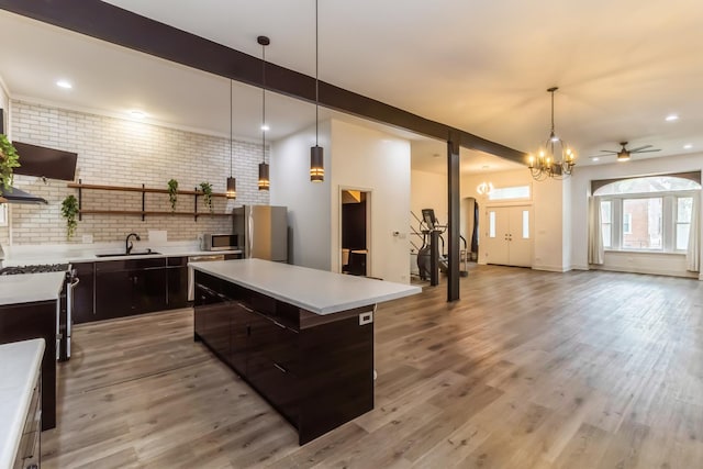 kitchen with a center island, ceiling fan with notable chandelier, beam ceiling, stainless steel appliances, and brick wall