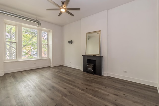 unfurnished living room with ceiling fan, a wood stove, and dark wood-type flooring