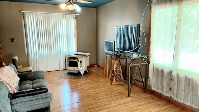 living room with ceiling fan, a wood stove, and light wood-type flooring