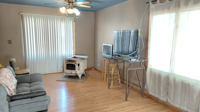 living room featuring light wood-type flooring, a wood stove, and ceiling fan