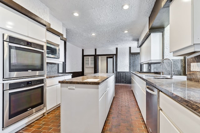 kitchen featuring a kitchen island, appliances with stainless steel finishes, white cabinets, backsplash, and sink