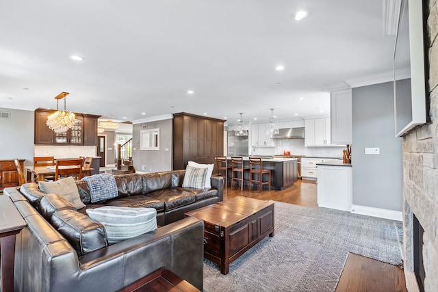 living room featuring an inviting chandelier, a stone fireplace, light hardwood / wood-style flooring, and crown molding