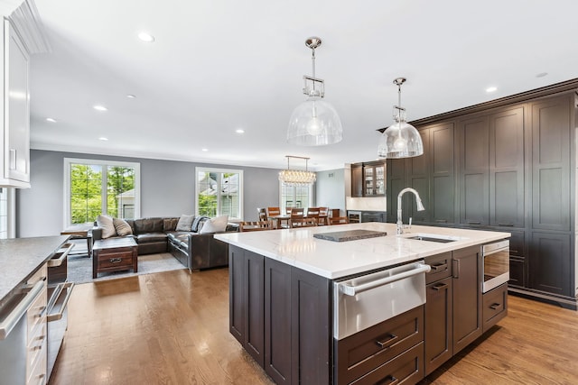 kitchen featuring dark brown cabinetry, a center island with sink, hardwood / wood-style floors, stainless steel microwave, and sink