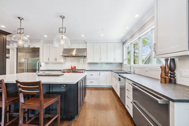 kitchen featuring a center island with sink, decorative light fixtures, wood-type flooring, sink, and appliances with stainless steel finishes