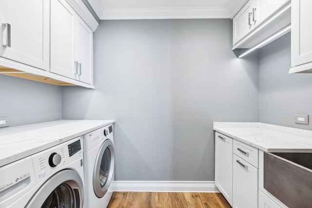 clothes washing area featuring ornamental molding, washer and clothes dryer, light wood-type flooring, and cabinets