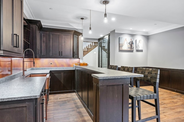 kitchen with crown molding, light wood-type flooring, dark brown cabinets, pendant lighting, and a breakfast bar