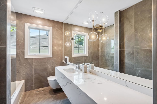 bathroom featuring a healthy amount of sunlight, oversized vanity, tile walls, and toilet