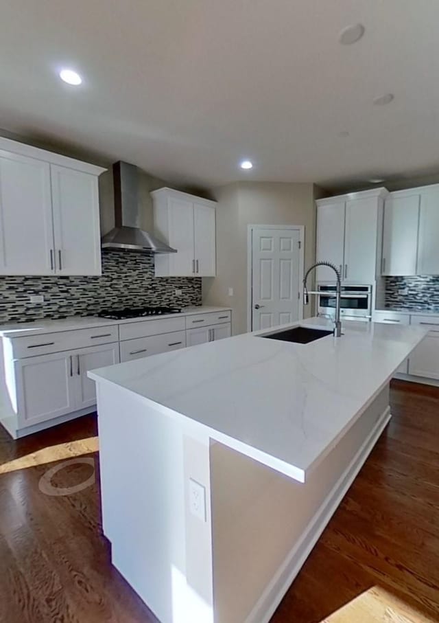 kitchen featuring white cabinetry, sink, wall chimney exhaust hood, dark wood-type flooring, and an island with sink