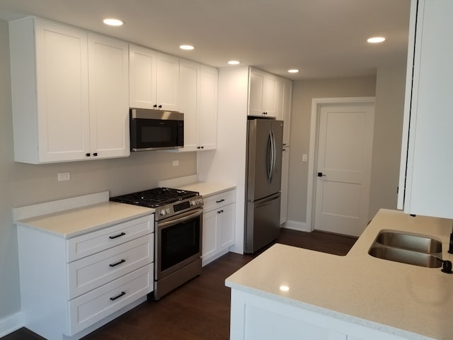 kitchen with light stone countertops, stainless steel appliances, dark hardwood / wood-style flooring, sink, and white cabinets